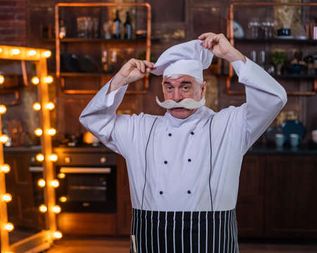 A friendly elderly male professional chef wearing an apron and a hatの写真素材
