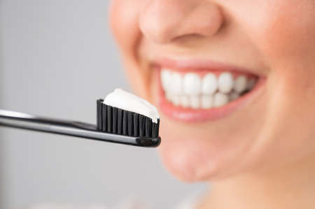 A woman with a snow-white smile holds a toothbrush with paste on a white background