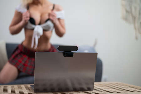A young woman dressed in a schoolgirl costume is engaged in virtual sex on a laptop. The web model...