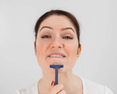 Caucasian funny woman shaves her face with a straight razor on a white background. Copy space.の写真素材
