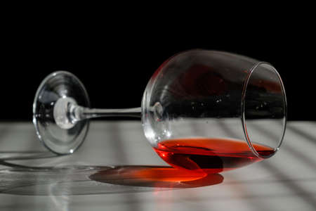 A glass of red wine lies on its side on a white table with a shade from the blinds.の写真素材