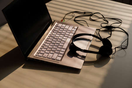 Headphones lie on a laptop keyboard on a white table. The shadow from the blinds falls on the desktop.の写真素材
