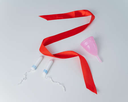 Tampon, pink menstrual cup and red satin ribbon on a white background. Means of intimate hygiene of a woman during mentruationの写真素材