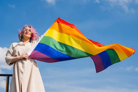 Caucasian woman with curly colored hair holding lgbt flag. Lesbian woman holding a rainbow flag...