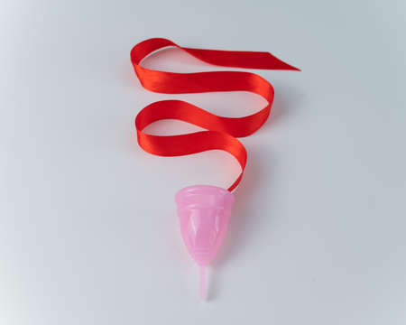 Pink menstrual cup and red satin ribbon on a white backgroundの写真素材