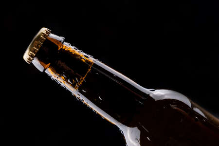 Dark glass beer bottle with condensation drops on black background.