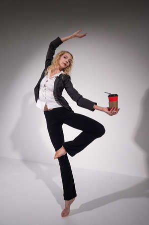 Graceful barefoot ballerina in a business suit jumping with a glass of coffee in her hands on a...