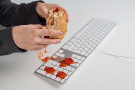 A faceless woman is eating a burger and dripping ketchup on the keyboardの写真素材