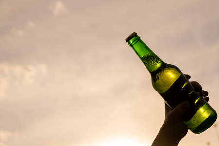 Woman holding bottle of beer outdoors against sky background.の写真素材