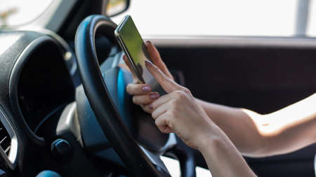 A faceless woman uses a mobile phone while driving a car. The girl uses the navigation in the smartphoneの写真素材