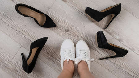 A woman chooses sports shoes instead of high-heeled shoes. Sneakers or shoesの写真素材
