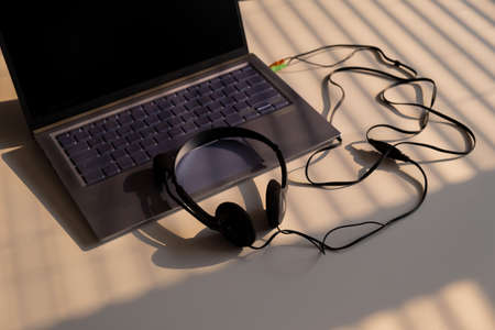 Headphones lie on a laptop keyboard on a white table. The shadow from the blinds falls on the desktop.の写真素材