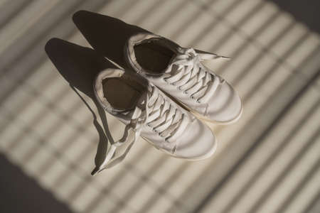 Close-up of womens white leather sneakers in the shade of the blinds.