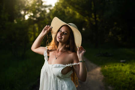Beautiful caucasian woman in a white dress and straw hat in the forestの写真素材
