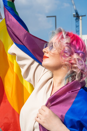 Caucasian woman with curly colored hair holding lgbt flag. Lesbian woman holding a rainbow flag outdoorsの写真素材
