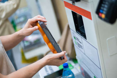 A woman scans products at a self-checkout counter. Close-up of female hands self buying groceries in the supermarket without a salesperson.の写真素材