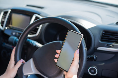 A faceless woman uses a mobile phone while driving a car. The girl uses the navigation in the...