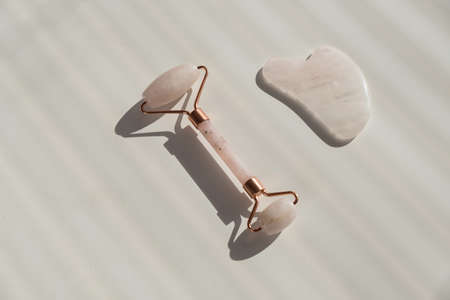 Pink guache scraper and roller on a white table. Equipment for self-massage and skin care for the...