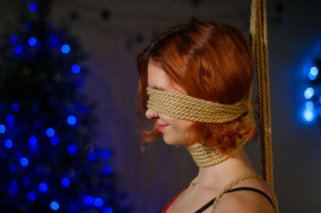 Girl in lace red underwear tied with ropes in Japanese shibari style at Christmas decorations.