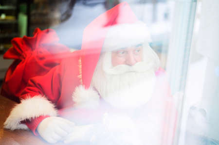 Santa Claus is sitting in a cafe. Outside view through the window.の写真素材
