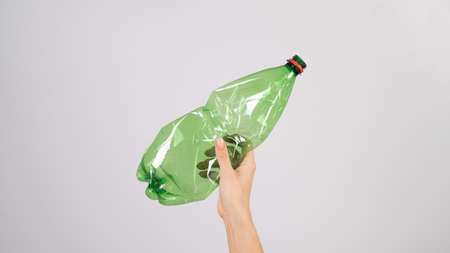 Close-up of female hand holding green plastic bottle on white background.