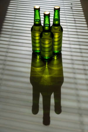 Three green glass beer bottles in the shade of the blinds.の写真素材