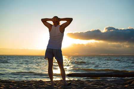 A humorous portrait of a brutal man in a T-shirt and boxers on the beach at sunsetの写真素材