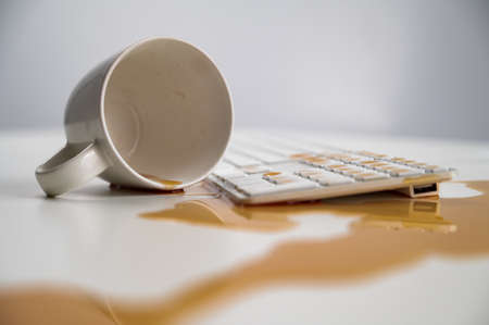 Spilled cup of black coffee on computer keyboard on white table.の写真素材