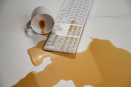 Spilled cup of black coffee on computer keyboard on white table.の写真素材