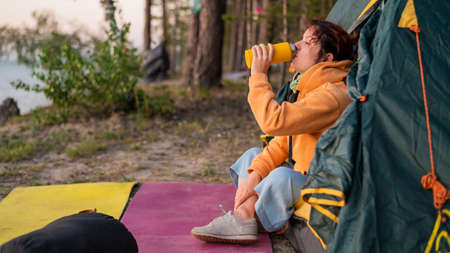 Caucasian woman drinking hot tea from a while resting in a tourist tent.