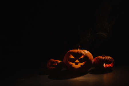 Pumpkins with carved grimaces and candles inside in the dark for halloween. Jack o latern in smoke.の写真素材