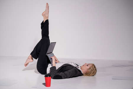 Barefoot ballerina dressed in a business suit poses for a laptop and drinks coffee. Flexible woman works at the computerの写真素材