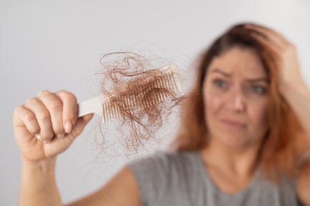 Caucasian woman with a grimace of horror holds a comb with a bun of hair. Hair loss and female alopecia.の写真素材