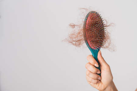 Close-up of a female hand holding a comb with a bun of hair on a white background. Hair loss and...