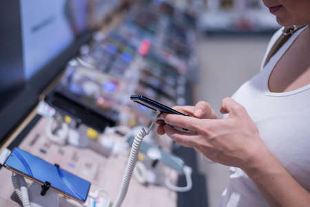 Faceless caucasian woman chooses a smartphone in an electronics store. Close-up of a female hand with a phone testerの写真素材