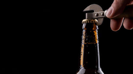 A man opens a bottle of beer from a dark glass with drops of condensation on a black background.の写真素材
