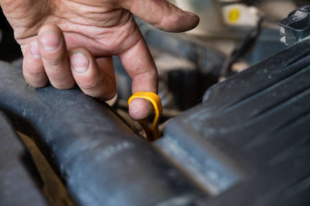 An auto mechanic pulls out a dipstick to check the oil level in a car engine.