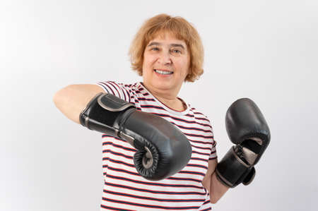 Elderly woman in fighting gloves in a defensive pose on a white background.の写真素材