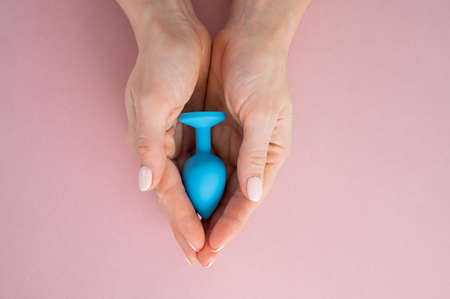 A woman is holding a blue anal plug on a pink background. Adult toy for alternative sexの写真素材