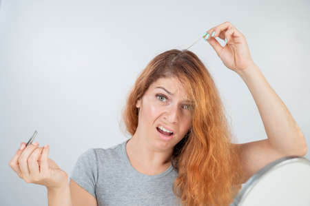 Caucasian woman finds gray hair and removes it with tweezers. Signs of aging.の写真素材