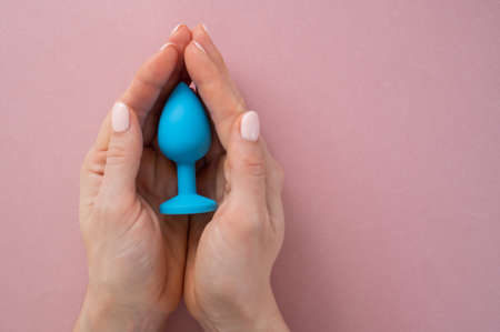 A woman is holding a blue anal plug on a pink background. Adult toy for alternative sexの写真素材