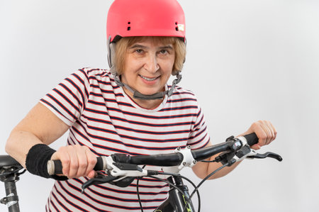 Elderly woman in pink helmet on a bicycle on a white background.の写真素材