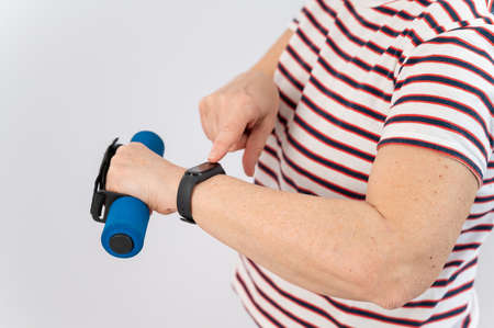 Elderly woman looking at fitness bracelet while exercising on white background.の写真素材