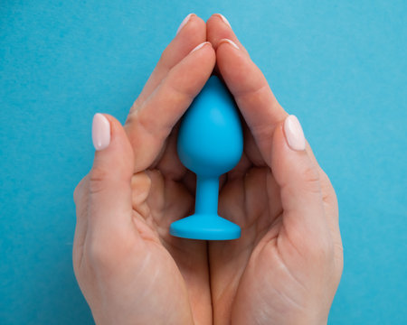 A woman is holding a blue anal plug on a blue background. Adult toy for alternative sexの写真素材