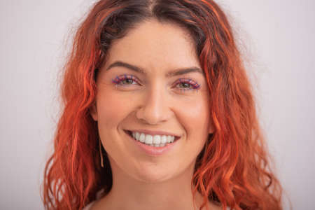 Portrait of caucasian red-haired woman with colored eyelashes on white background.