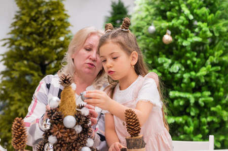 Elderly caucasian woman making pine cones decoration for christmas with two granddaughters