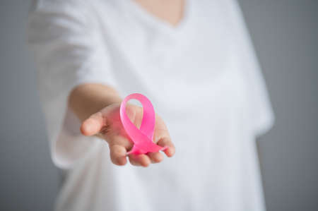 A faceless woman wearing a white t-shirt holds a pink ribbon as a symbol of breast cancer on a white background.の写真素材