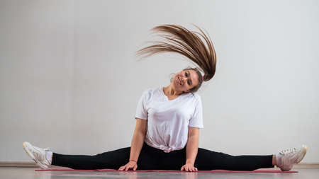 A young flexible fat woman sits in a transverse twine and waves her hair against a white backgroundの写真素材