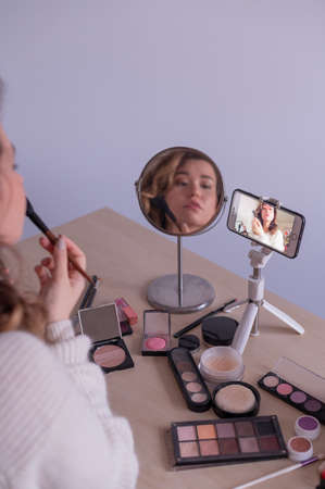 Caucasian woman leads an online make-up lesson for herself on her mobile phoneの写真素材