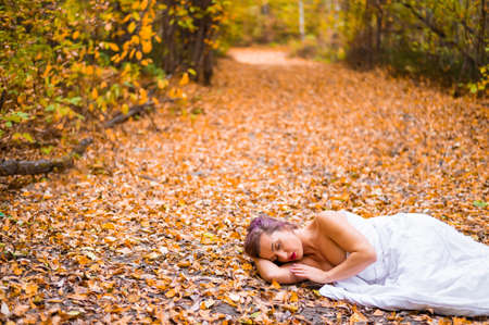 Caucasian woman lies in the autumn forest under a blanket. Nude girl in a leaf fallの写真素材